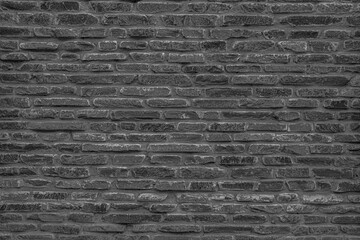 The black wall is made of uneven black gloomy stones. Abstract dramatic background.