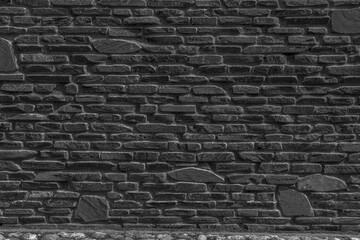 The black wall is made of uneven black gloomy stones. Abstract dramatic background.