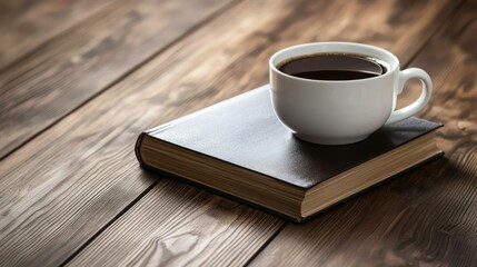 Obraz premium Close-up of a white ceramic coffee cup filled with black coffee placed on a closed hardcover book on a rustic wooden surface in a cozy warm ambient setting
