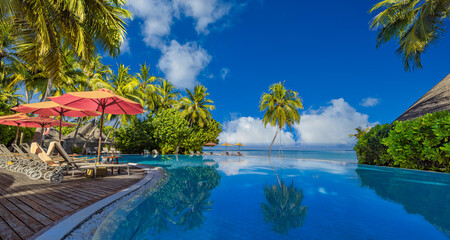 Luxury infinity swimming pool in tropical hotel resort. Palm trees poolside lounge chairs umbrellas. Leisure exotic travel destination, summer tourism beach holiday. Stunning sea sand beach landscape