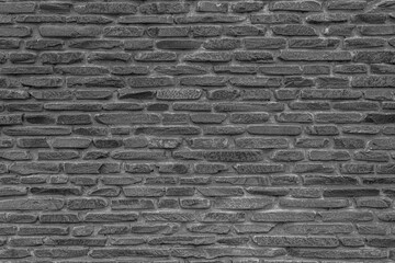 The black wall is made of uneven black gloomy stones. Abstract dramatic background.