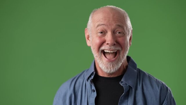 A middle-aged man with a white beard and joyful expression stands in front of a green screen, showcasing his friendly demeanor and relaxed attire.