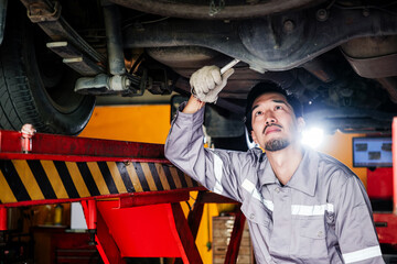 Automobile technician inspecting the underside of a lifted vehicle in a service garage, demonstrating hands-on diagnostics, maintenance, and professional car repair in a mechanical workshop.