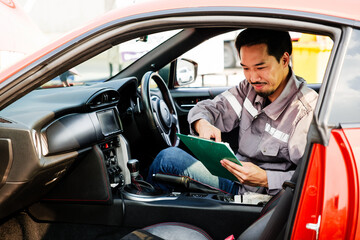 Auto service technician reviews inspection checklist inside a red car at a service center, representing professional maintenance, diagnostics, and customer-oriented automobile repair service.