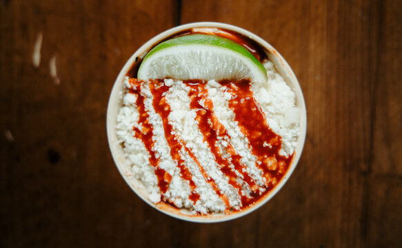 A Cup of Elote with Cheese and a Lime Wedge Shot from Above