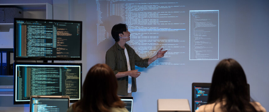 Asian man presents code using a projector during a software development meeting or coding workshop, guiding attendees through problem-solving and programming concepts in an educational setting.