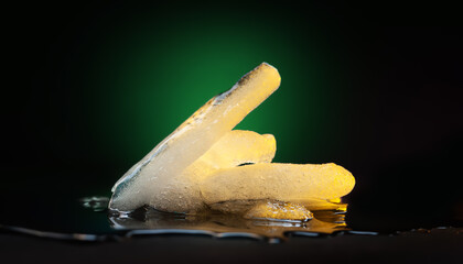 Ice melting. Pieces of melting ice on a dark background. Colored green-yellow backlight. Selective focus