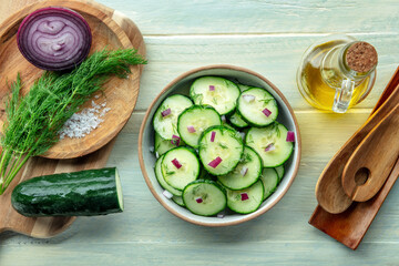 Cucumber salad with olive oil, dill, and red onion, overhead flat lay shot on a rustic wooden table