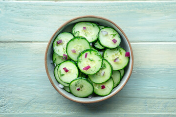 Cucumber salad with dill and red onion, overhead flat lay shot on a rustic wooden table in a bowl