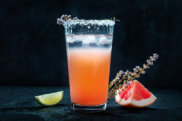 Salty Dog cocktail with fresh grapefruit juice, lime juice, and thyme, side view with fresh fruit on a black background