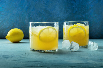 Glasses of lemonade, a mocktail with lemon juice, on a blue background, summer cold drink, side view with copy space