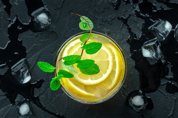 A glass of fresh lemonade, a mocktail with lemon juice, on a black background, overhead flat lay shot with mint