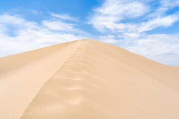 Golden sand dunes of Ica desert under a clear blue sky in Huacachina, Peru