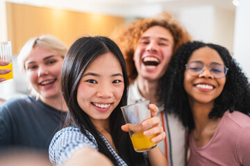 Group of cheerful young multiethnic friends enjoying a lively moment while taking a selfie and sipping refreshing juice in a cozy kitchen