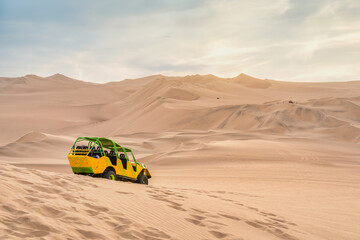 A colored dune buggy on the golden sand dunes of the Ica Desert near Huacachina, Peru at sunset.