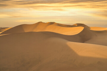 Ica desert landscape at sunset with smooth golden sand dunes near Huacachina, Peru.