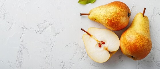Three ripe pears, one sliced in half, on a light textured surface with a green leaf nearby.