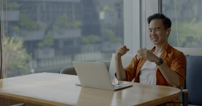 Senior Asian businessman wearing headset celebrates success during online meeting in modern co-working space. Remote work and business communication concept.	
