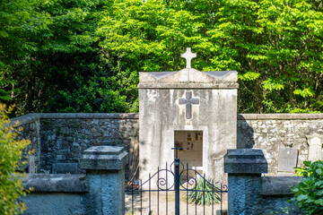 old stone crypt with prominent cross, surrounded by lush green foliage, ancient traditional religious heritage, Historic Burial Site