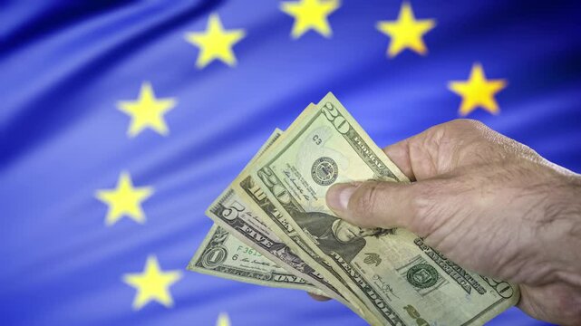 Hand holding some US dollars banknotes in front of a European Union flag, concept of trade war, taxes and tariffs and the 899 Act.