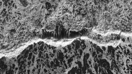 Aerial black and white view of view, depicting the dynamic patterns of breaking waves and sea foam...