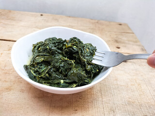 Selective focus. Daun singkong or Cassava leaf curry is a traditional Indonesian dish, made from boiled cassava leaves, seasoning with coconut milk and spicy curry spices. 