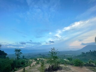 A peaceful morning sky with soft blue hues and gentle clouds above a green forest. Ideal for background use, graphic design, presentations, and travel content.