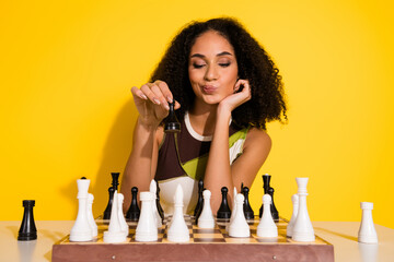 Young woman enjoying chess against a vibrant yellow background, expressing joy and contemplation