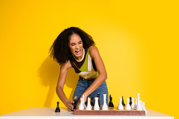 Stylish young woman passionately engaged in a chess game, expressing emotion against bright yellow...