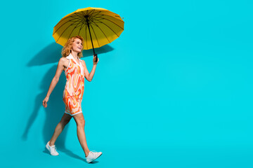 Happy young woman with vibrant style holding a yellow umbrella against a teal background, embodying...