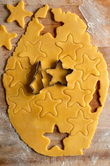 Raw and rolled out shortcrust pastry, cookie cutters and biscuits arranged on a wooden cutting board.