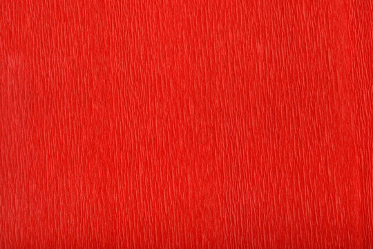 A detailed close-up shot captures the textured surface of a vibrant red crepe paper, showing its distinct parallel wrinkles