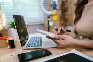 A confident female entrepreneur manages her online business from home, handling packages, sales, and logistics with technology and a smile.