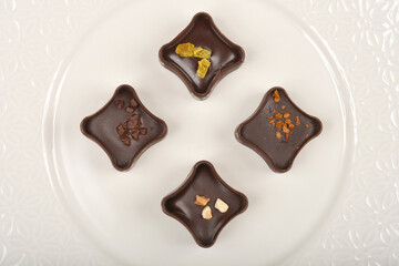Top-down shot features four dark chocolate pralines, each with unique toppings, arranged...