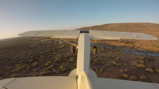 Extreme wide tail view of a bushcraft plane flying over a dried up riverbed in the savanna at kenya