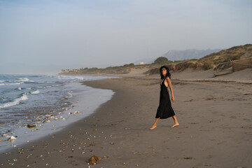 Brunette Woman in Black Dress Walking Along the Beach