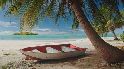 Small red and white boat resting on a pristine white sand beach under the shade of palm trees in Aitutaki, Cook Islands, with turquoise waters and a small island in the background