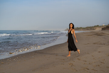 Brunette Woman in Black Dress Walking Along the Beach