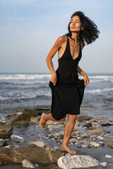 Brunette Woman in Black Dress Facing the Sea on Rocks