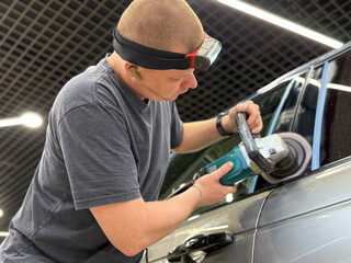 Car detailing series: Polishing grey car close-up. The process of polishing the car body in close-up. Master repairman polishing fender of car in workshop using rotary polishing machine.
