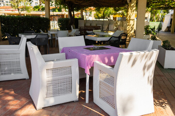 Empty outdoor table with pink cloth and wicker chairs. Summer hospitality, shaded relaxation, and peaceful cafe ambiance.