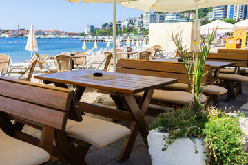 Wooden benches and tables at beach cafe under umbrella. Coastal hospitality, summer relaxation, and outdoor seating near sea.