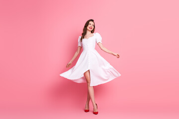 Stylish young woman in white dress posing against pink background with elegance and joy