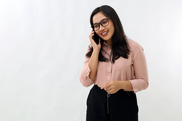 Friendly and cute young Asian girl with glasses looks relaxed, smiles happily, holds smartphone, talks casually on the phone, good cellular connection, stands on white background.
