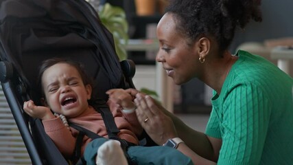 Medium shot of caring African American mother giving pacifier to baby son, soothing in stroller indoors - Powered by Adobe