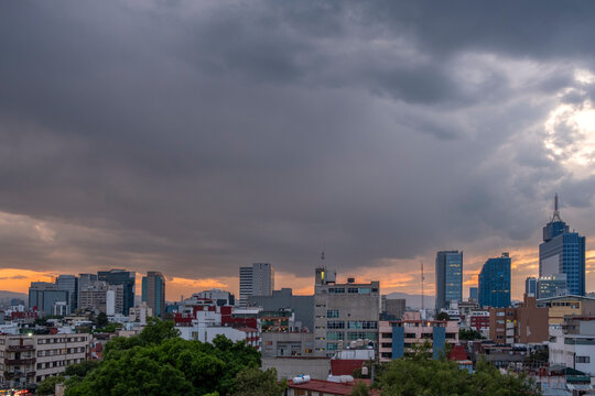 City skyline with dramatic clouds and warm sunset light, Colonia del Valle, Mexico City, elevated perspective with urban density and mountain background