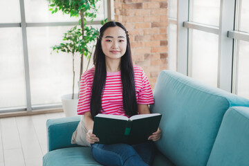 Young Woman Reading a Book on a Sofa in a Bright and Cozy Living Room Setting