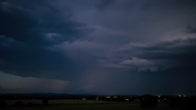  Time-lapse of a powerful thunderstorm at night, with dark storm clouds churning across the sky. Multiple bolts of lightning flash intermittently, illuminating the clouds and casting dramatic shad.