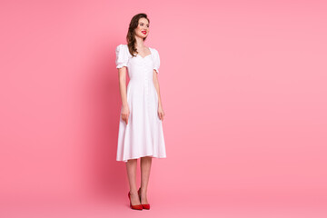 Charming young woman in white dress smiling confidently against a pink background in a stylish and elegant posture