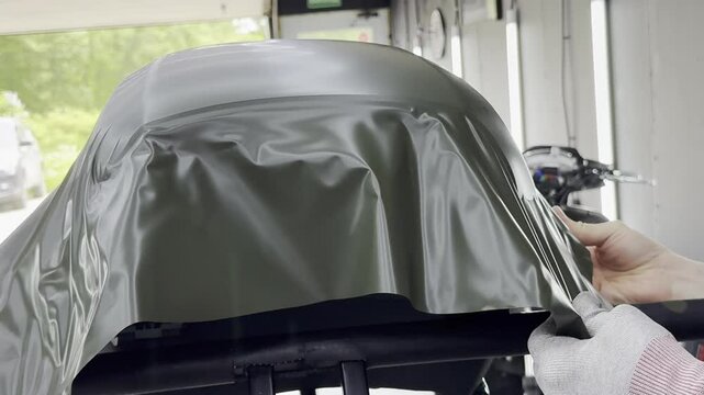 A specialist in wrapping a car with green khaki colored vinyl or ppf film in the process of work. Car wrapping specialists cover the car with green vinyl film. Khaki green vinyl foil. Selective focus.